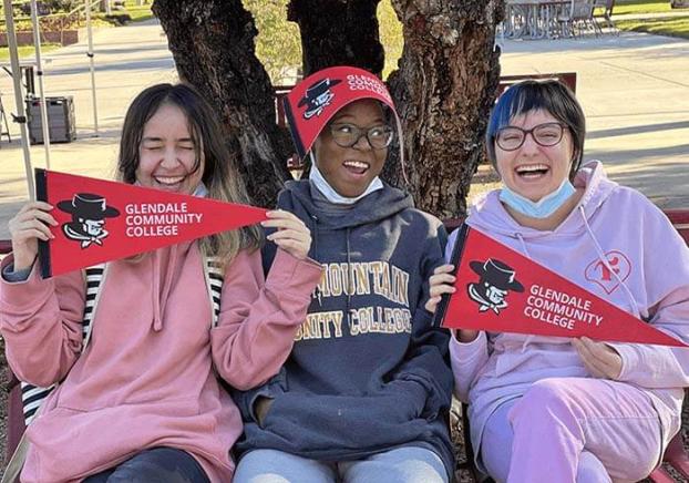 Three students sitting on the campus lawn with their gaucho pennants