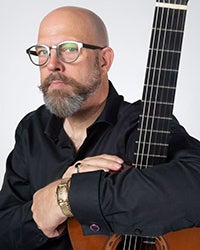 A picture of GCC Guitar Program Director Chuck Hulihan holding an acoustic guitar.