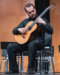 A picture of a student playing the acoustic guitar.